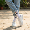 Person wearing white sneakers, light blue jeans, and striped socks on a wooden floor.