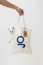 Person holding a tote bag with a cat peeking out, featuring a blue logo and a tag.